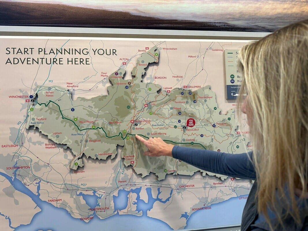 Woman points to a map of a hiking trail through towns like Winchester, Petersfield, and Midhurst.