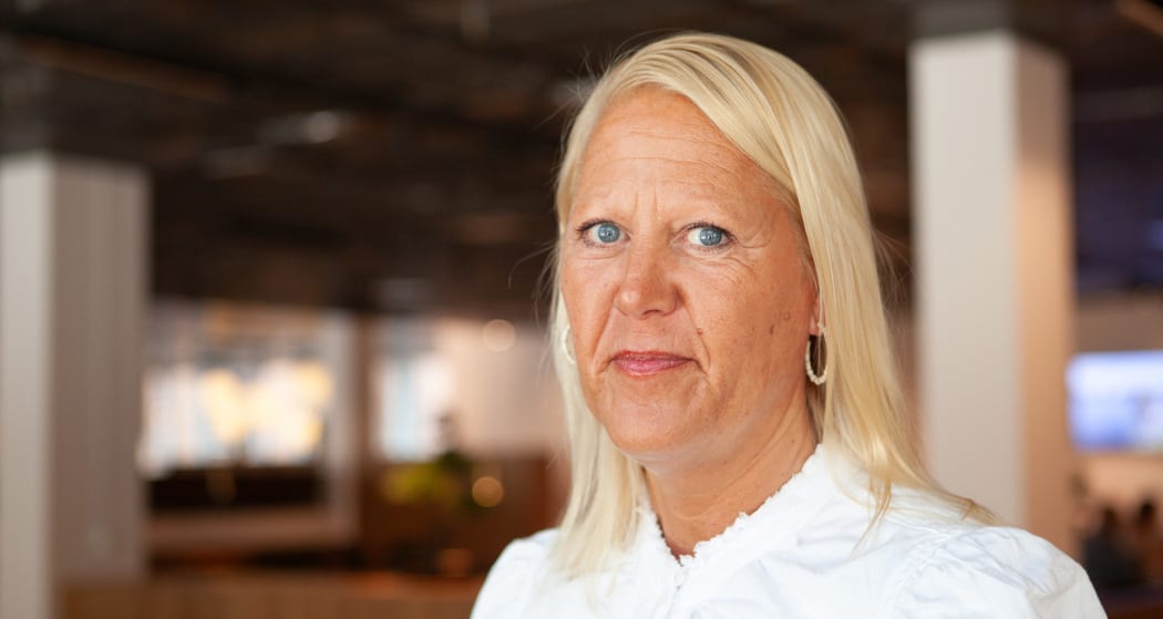 Headshot of a blonde woman with blue eyes, wearing a white shirt and hoop earrings, looking at the camera.