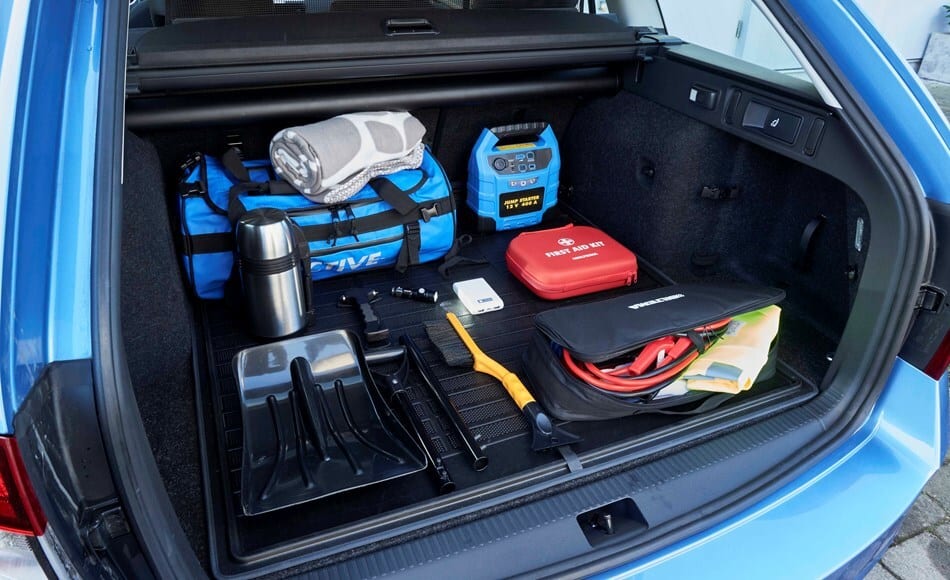 Car trunk packed with winter emergency kit: jump starter, first aid, shovel, and blanket.