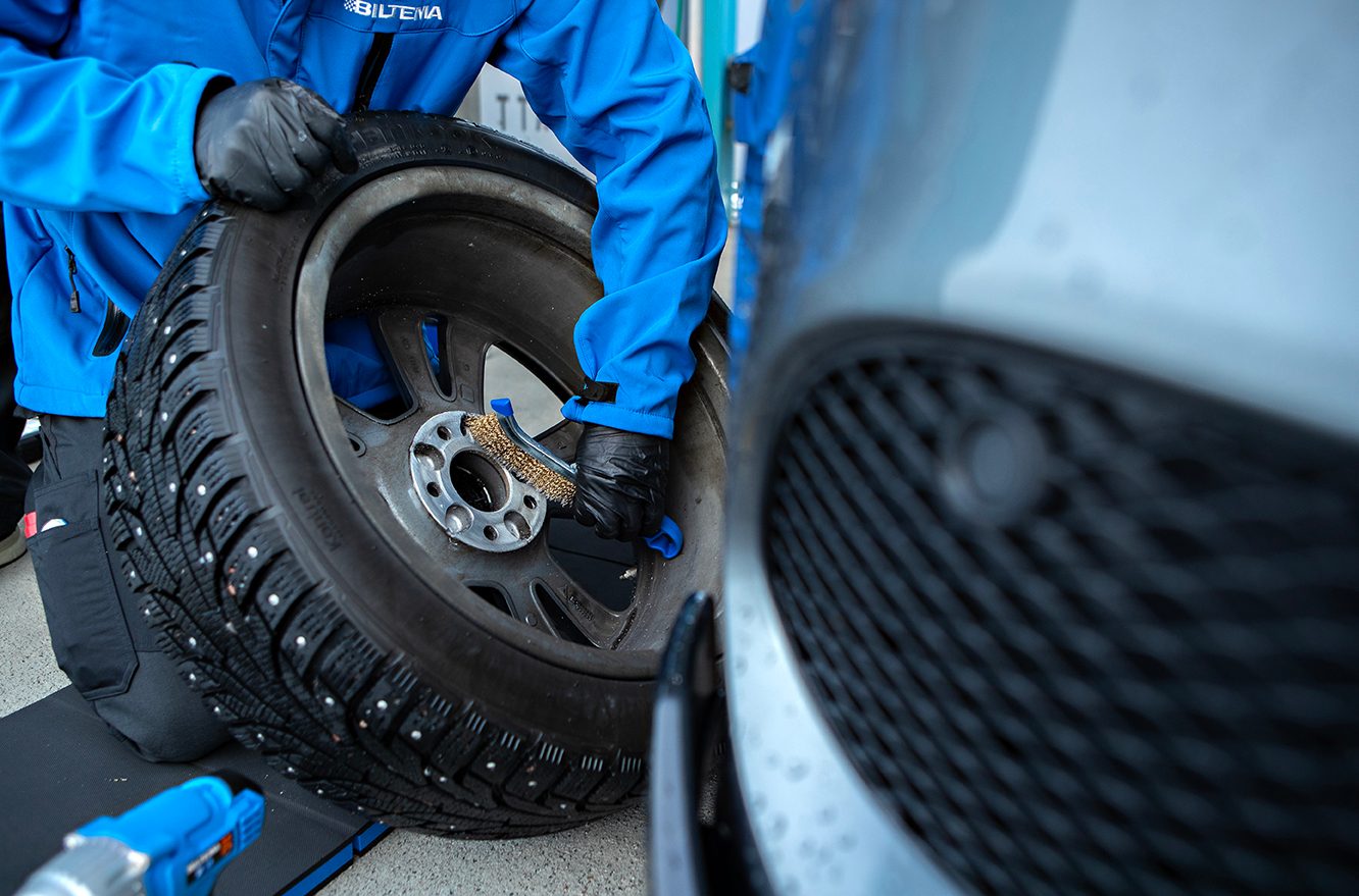 Person in blue jacket and gloves brushing a studded car wheel.