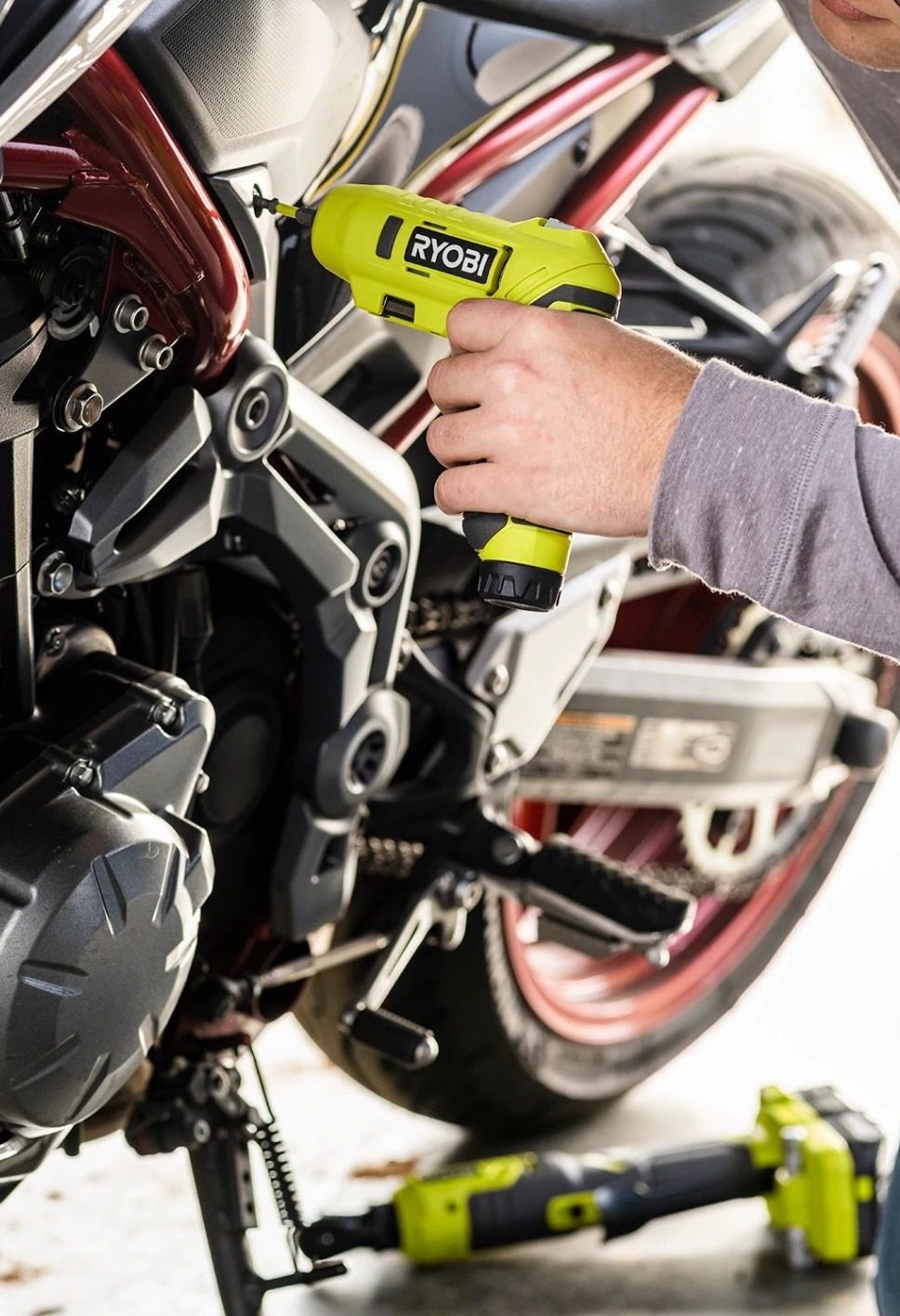 A person uses a green Ryobi cordless screwdriver to work on a motorcycle engine or frame.