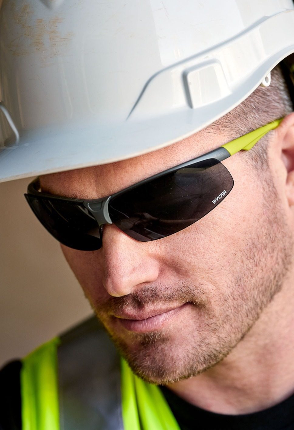 Close-up of a construction worker wearing a white hard hat and Ryobi safety glasses.