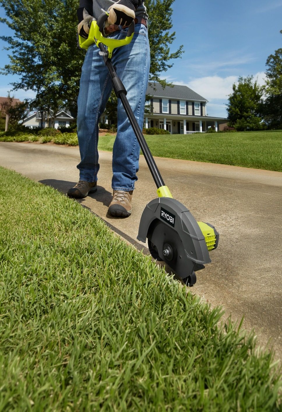 Person edging grass along a sidewalk with a Ryobi edger in front of a house.