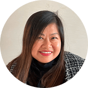 Headshot of a smiling Asian woman with long dark hair, wearing a black top and a patterned jacket.