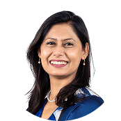 Smiling South Asian woman with dark hair, wearing a blue top and pearl earrings.