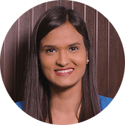 Headshot of a smiling young woman with long dark hair, wearing a blue top, against a brown background.