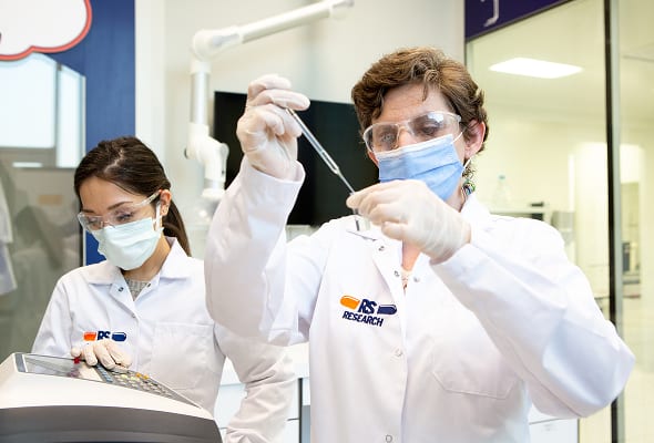 Two scientists, wearing lab coats, masks, and safety glasses, conducting experiments in a laboratory.