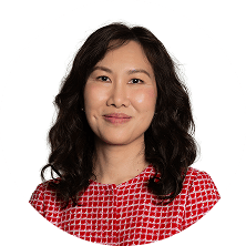 A smiling Asian woman with dark, wavy hair in a red and white patterned top.