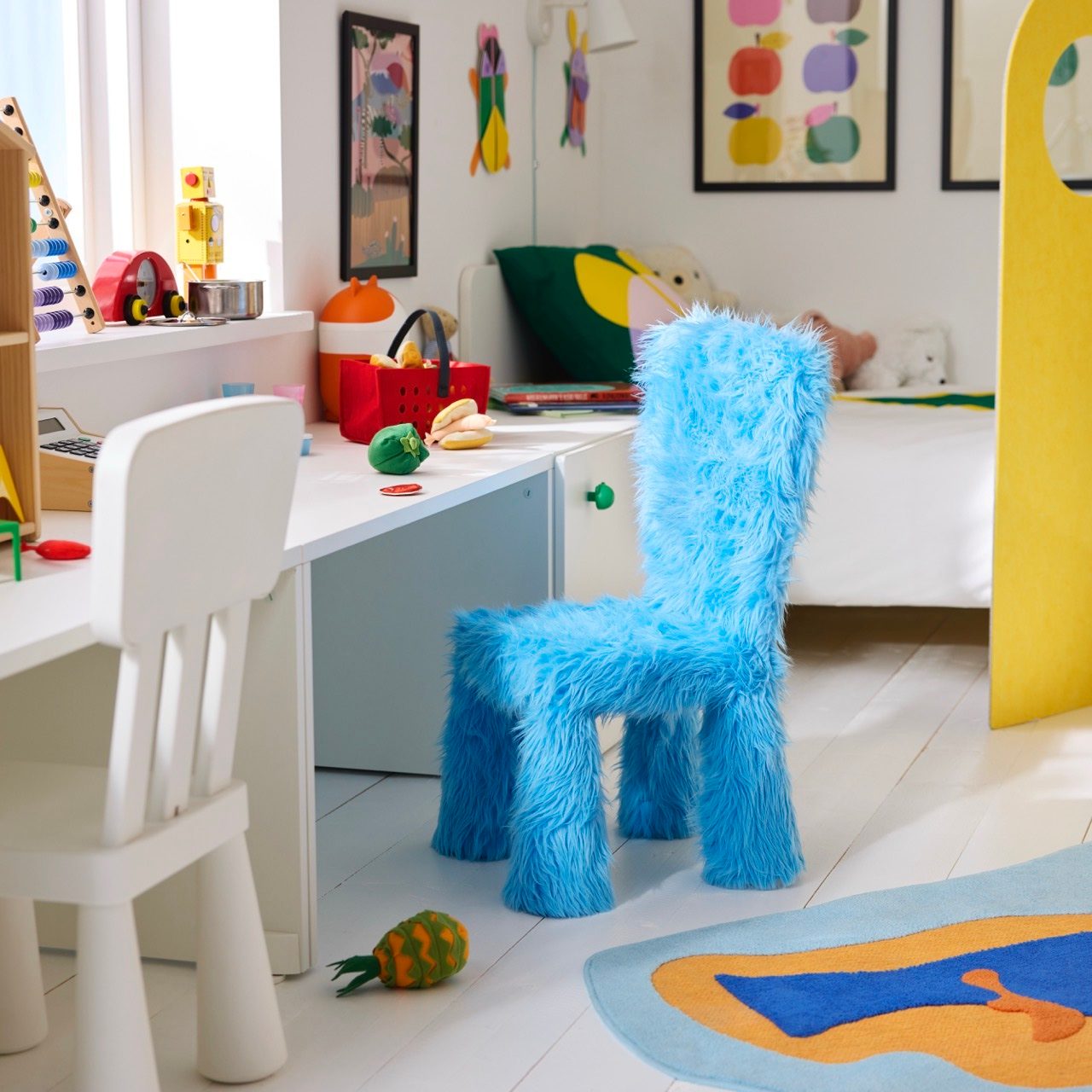 A vibrant child's room featuring a bright blue furry chair at a white desk, surrounded by colorful toys.