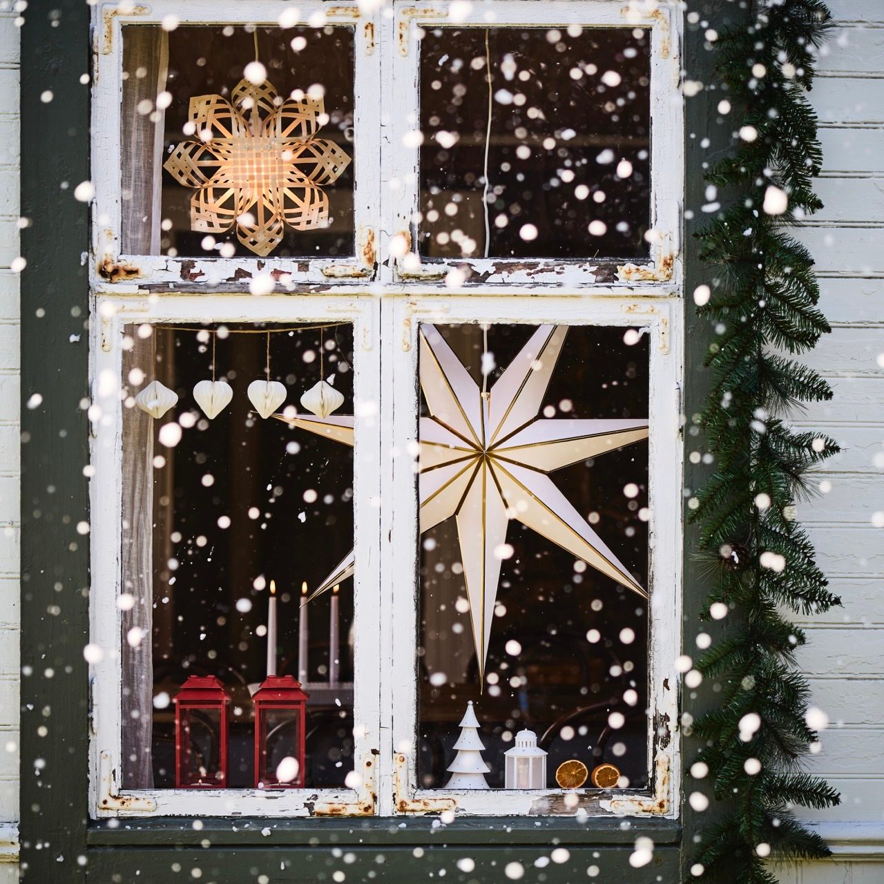 Old window decorated for Christmas with illuminated stars, lanterns, garland, and falling snow.