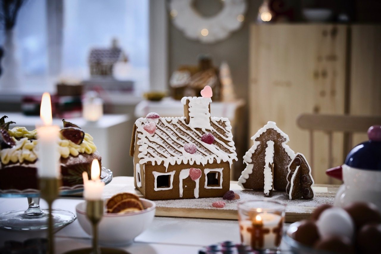Festive table with a gingerbread house, trees, cakes, and lit candles.