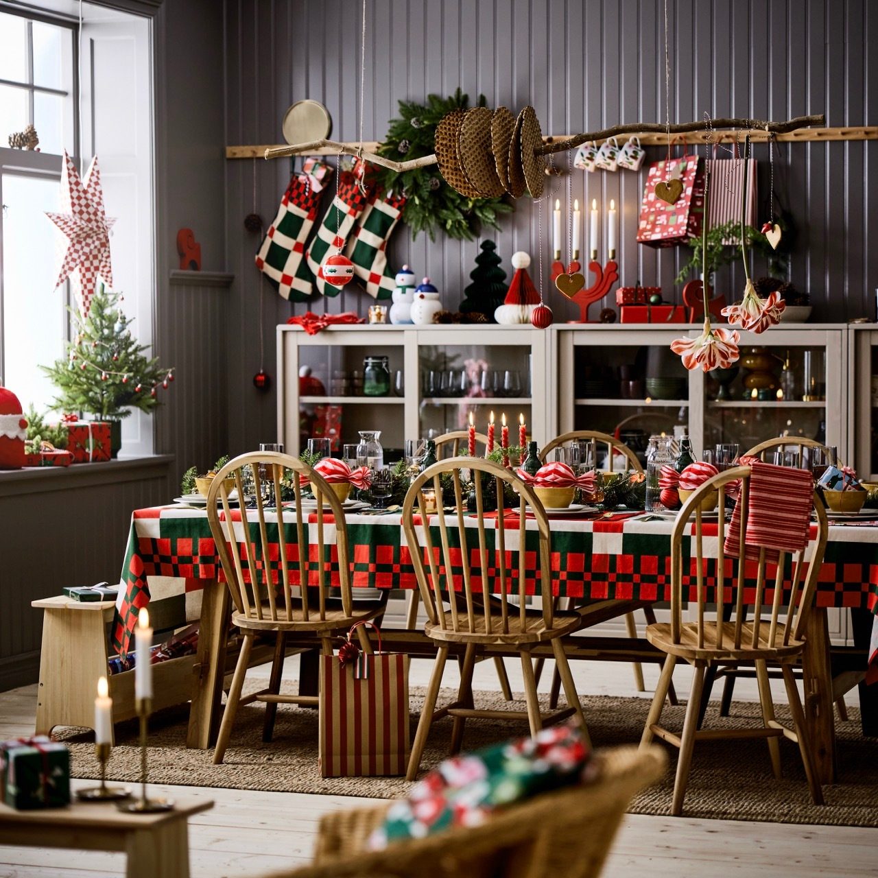 A festive dining room decorated for Christmas with a red and green plaid table, wooden chairs, and holiday decor.