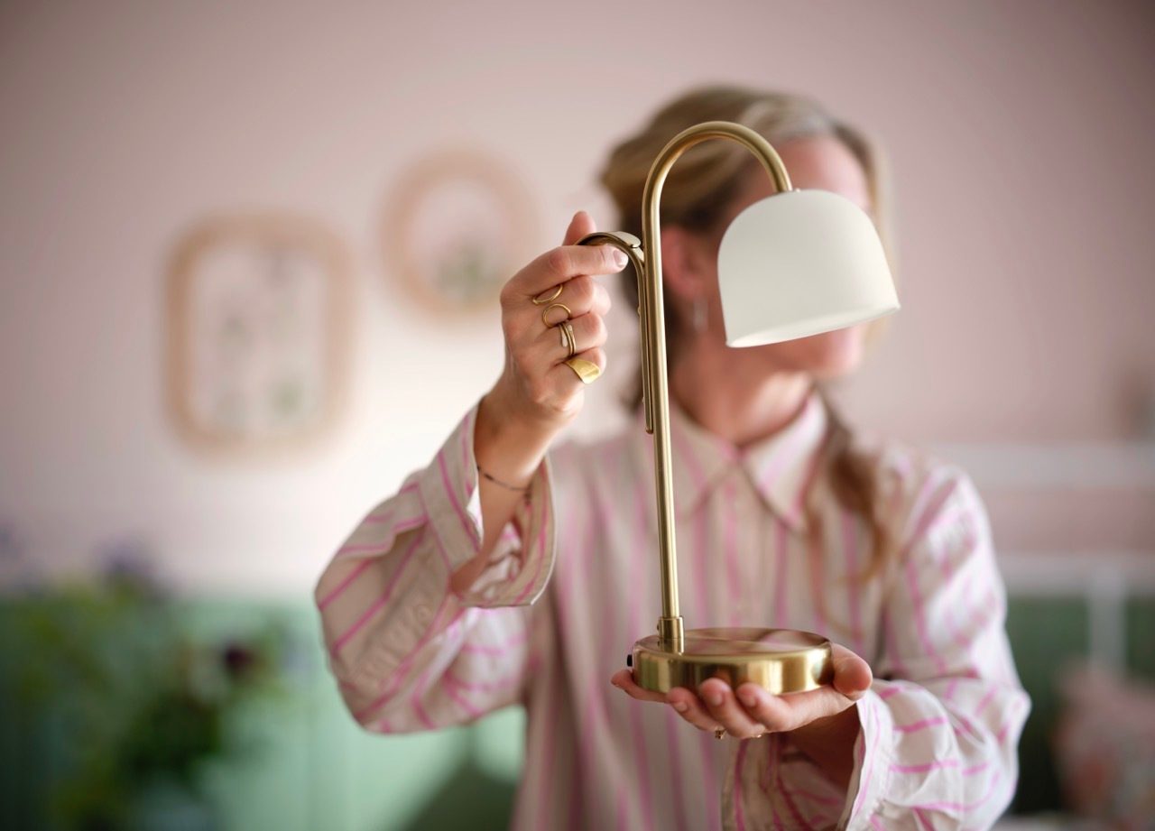Person holding a small gold lamp with a white shade.