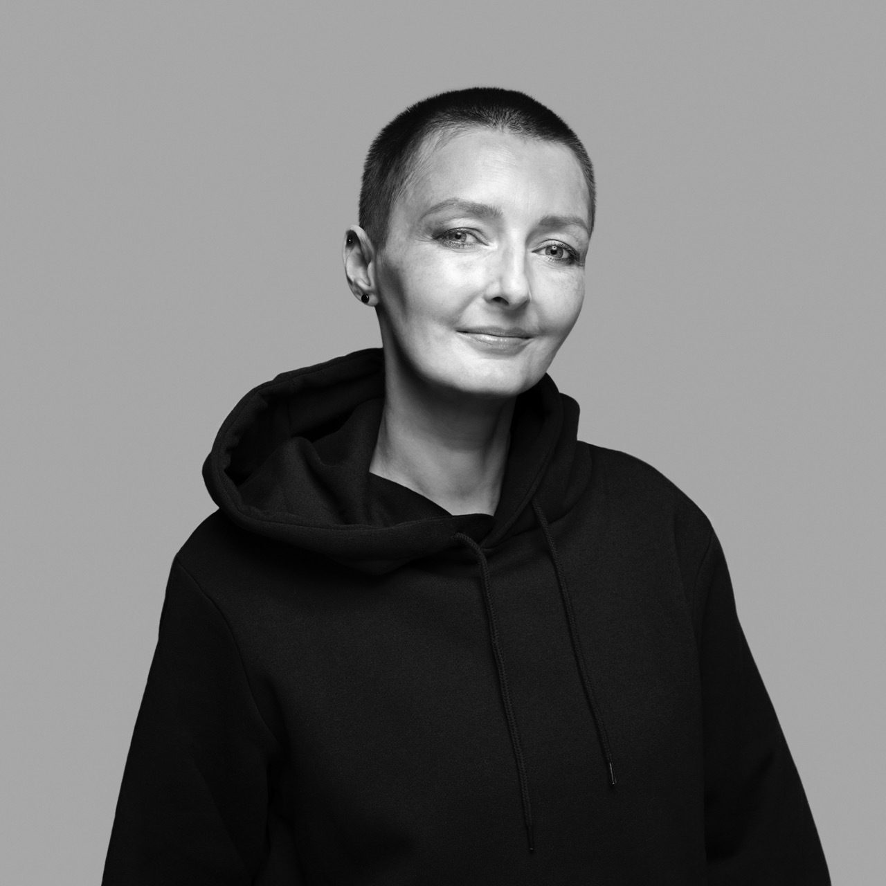 Smiling woman with buzz cut in black hoodie, black and white portrait.