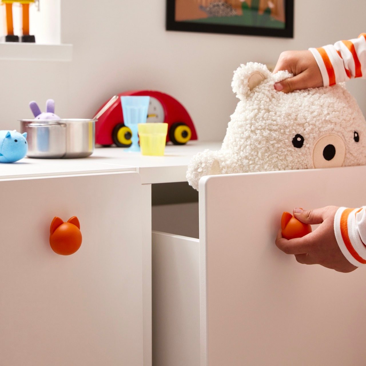 Child playing with a white bear, opening a drawer with an orange fox knob.