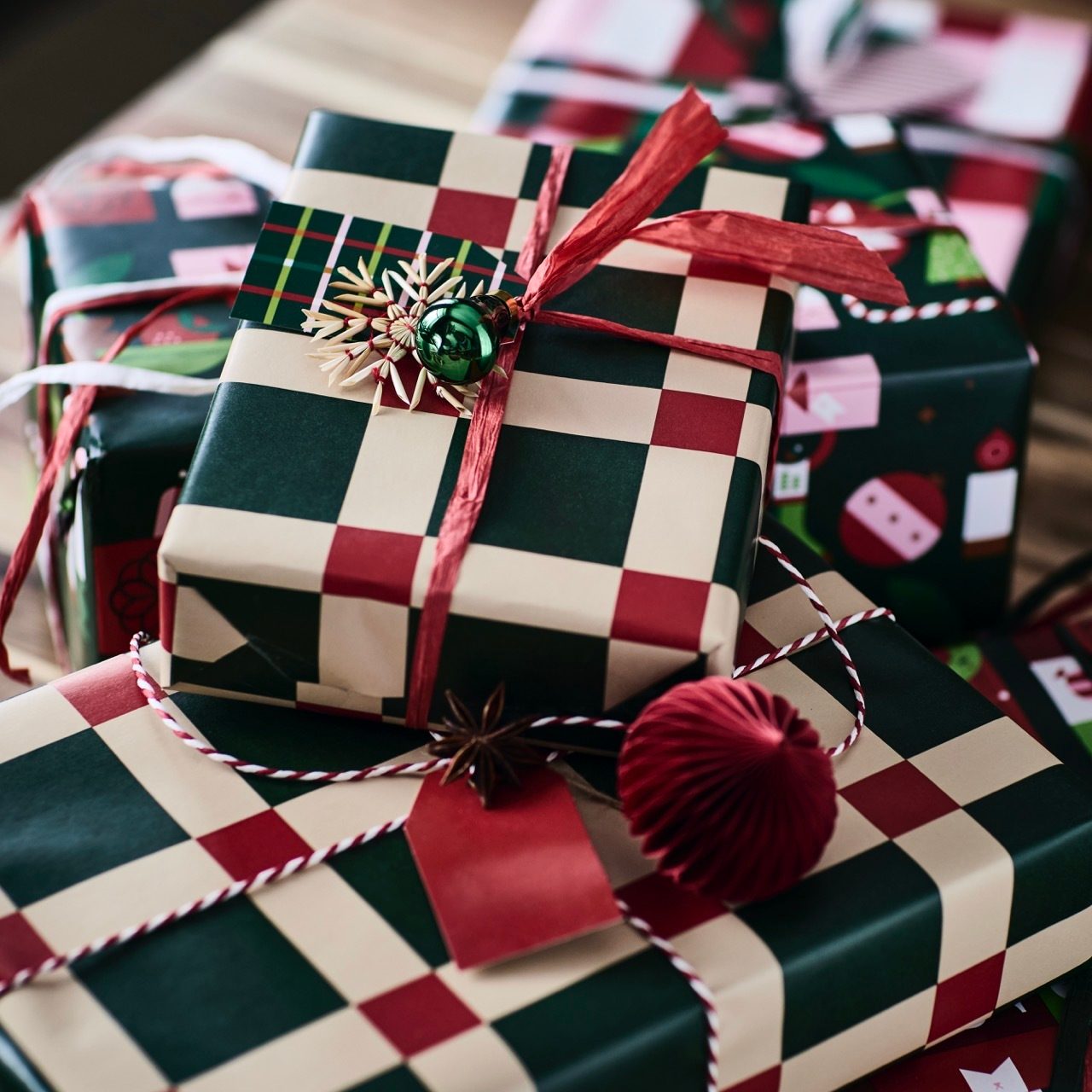 Christmas gifts in checkered and patterned wrap with red ribbons, ornaments, and star anise.