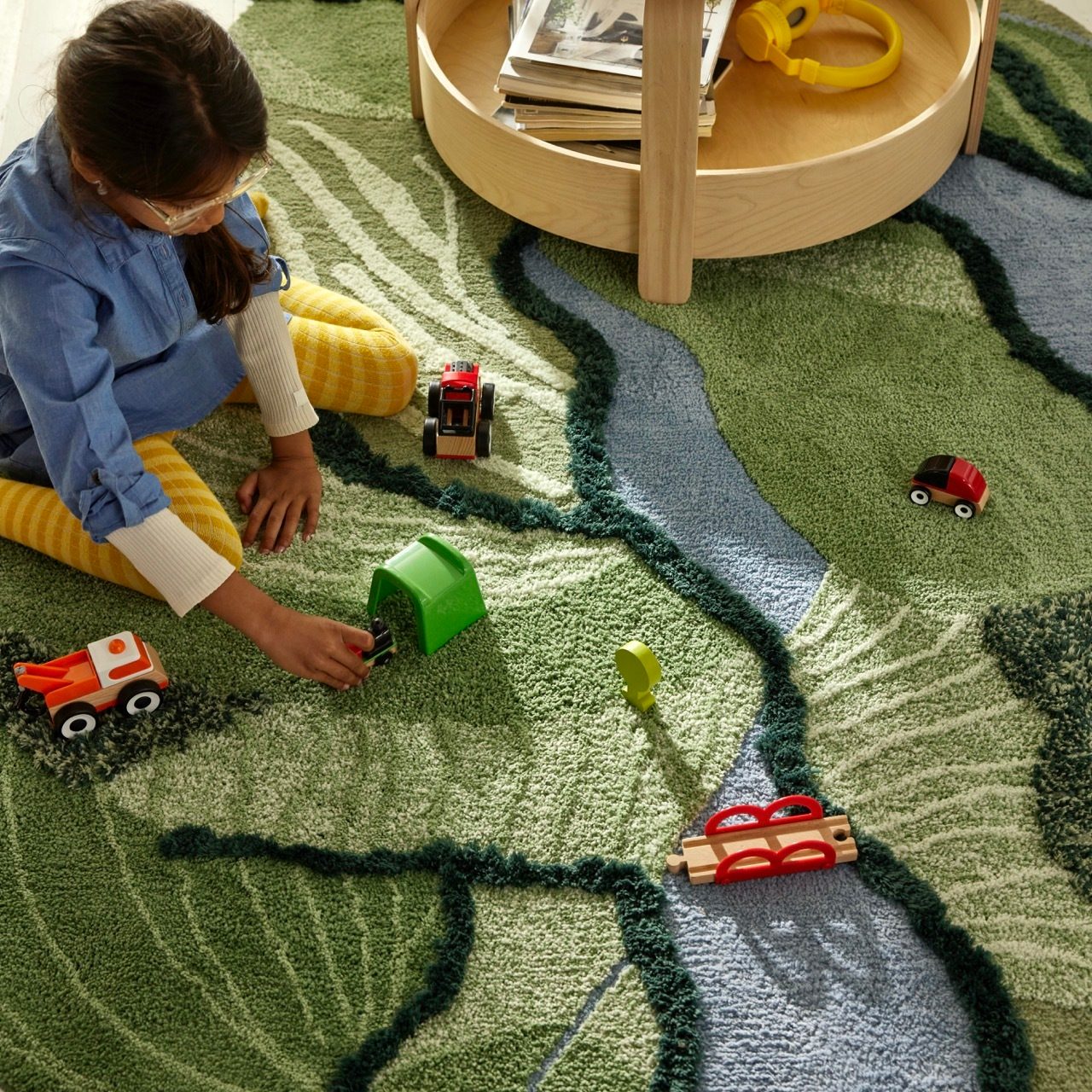 Child playing with wooden toys on a green rug with a blue river design.