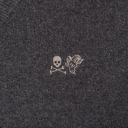 Close-up of dark grey knit fabric with embroidered skull and crossbones and winged creature.