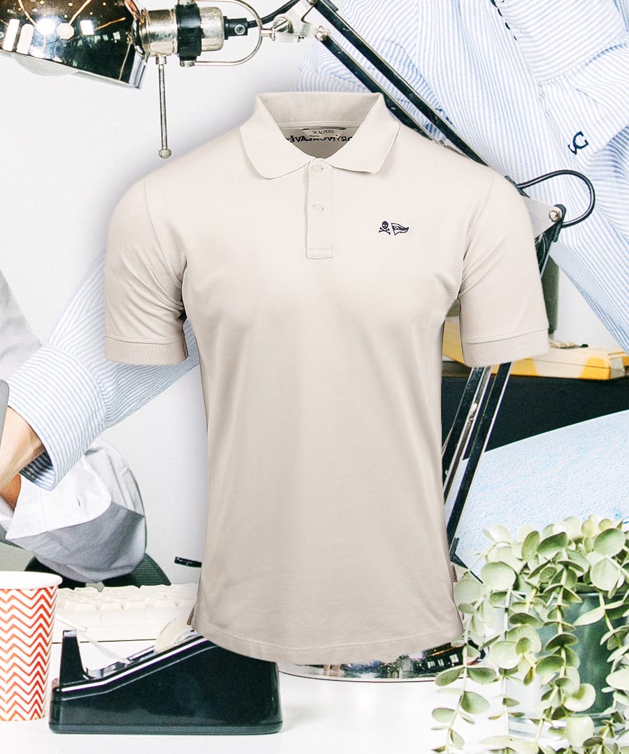 Light beige polo shirt with a skull and flag logo, against a background of office items.
