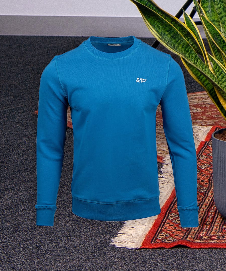 Blue long-sleeve sweatshirt with a small white emblem on the chest, displayed against a textured background.