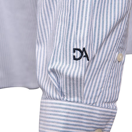 Close-up of a blue and white striped shirt sleeve featuring "DA" embroidered in dark thread.