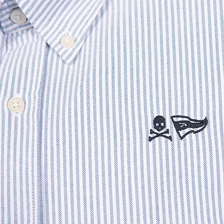 Close-up of a blue and white striped shirt featuring skull and crossbones and flag embroidery.