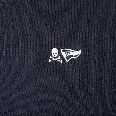 Close-up of a dark blue knitted fabric featuring white embroidered skull and crossbones and flag logos.