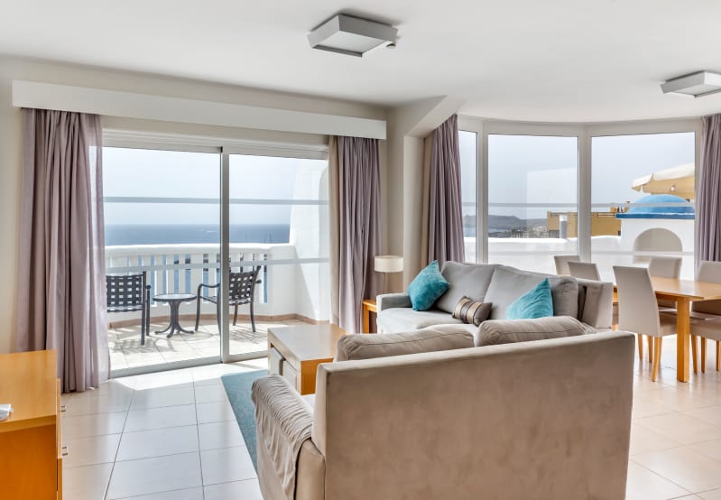 Bright living room with ocean-view balcony, sofas, and dining area.