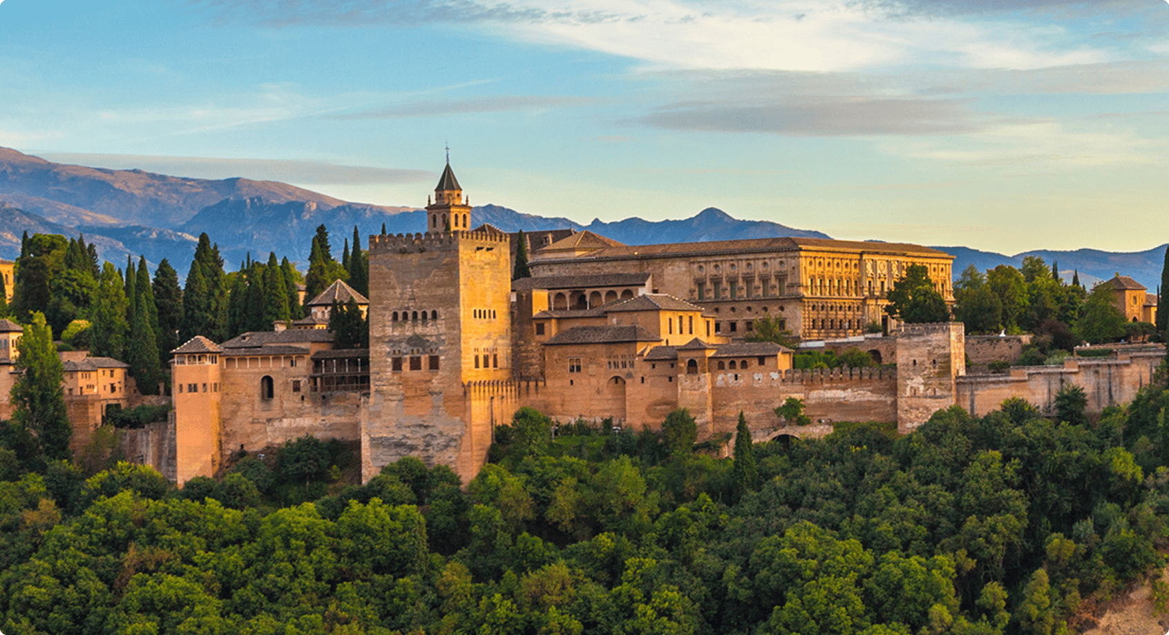 Alhambra palace and fortress complex in Granada, Spain, surrounded by trees and mountains.