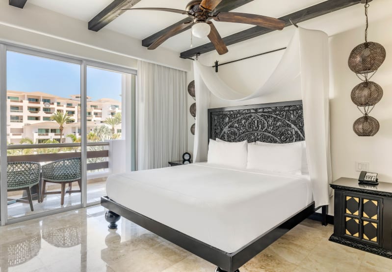 Luxurious bedroom with ornate bed, private balcony, palm tree view, and stylish ceiling fan.