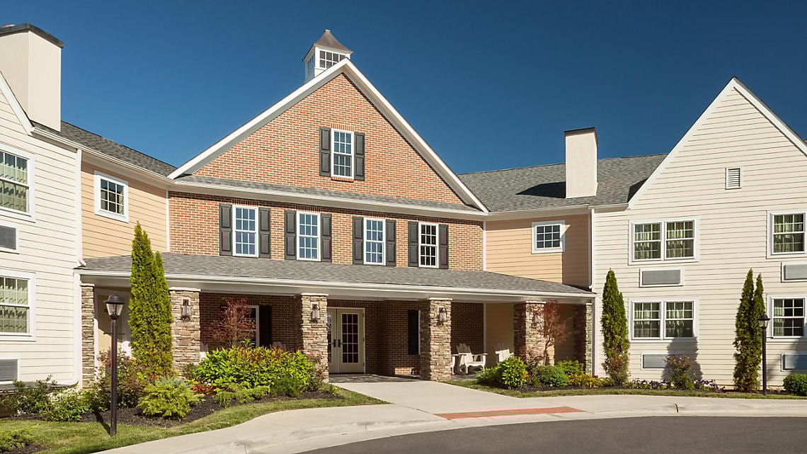 Multi-story building with brick and siding, a covered entrance, green landscaping, under a clear blue sky.