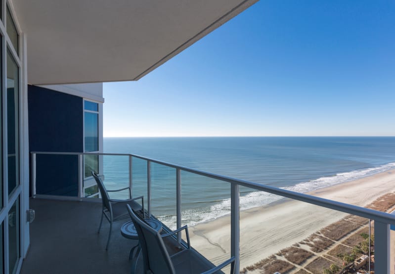 Balcony with chairs, overlooking the ocean and a sandy beach.