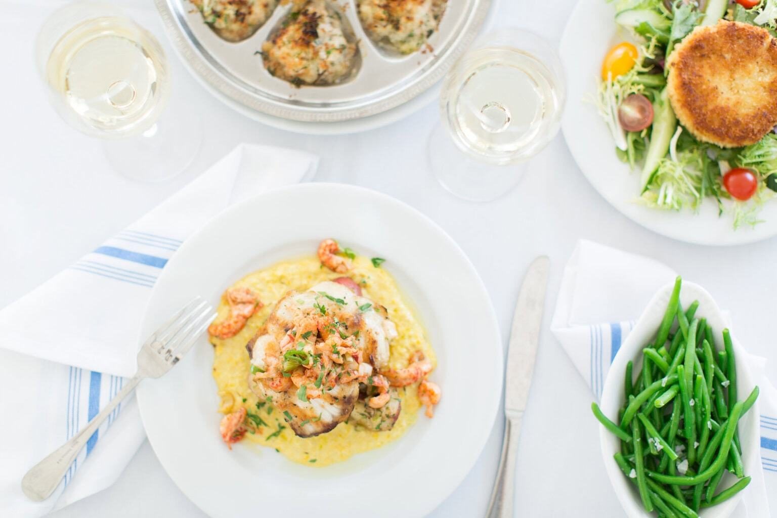 Seafood dinner: fish on grits with shrimp, baked oysters, crab cake salad, green beans, white wine.