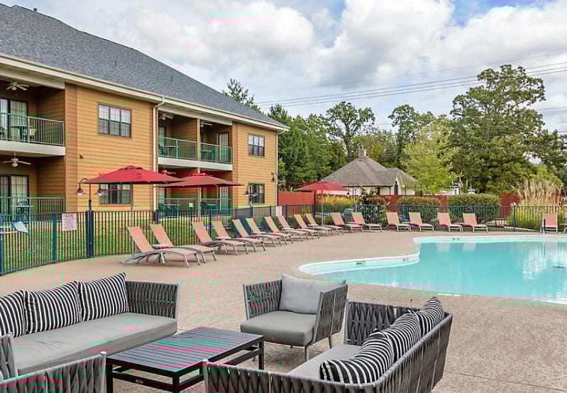 Outdoor pool area with a building, lounge chairs, red umbrellas, and patio seating.