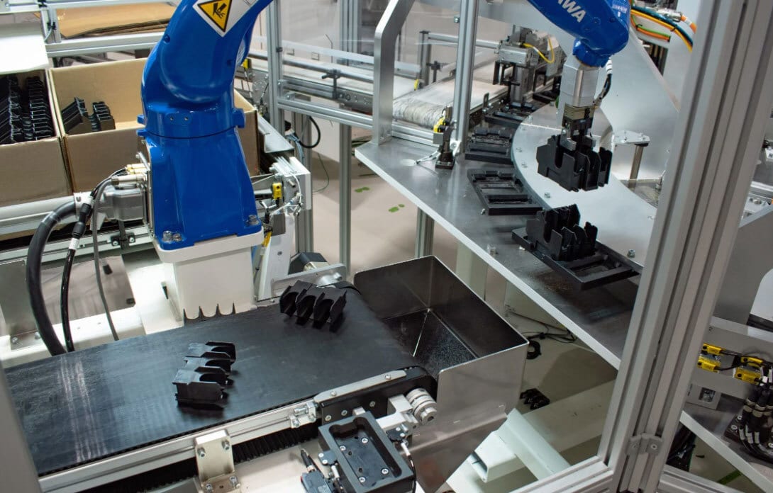 Robotic arm manipulating black components on a factory assembly line.