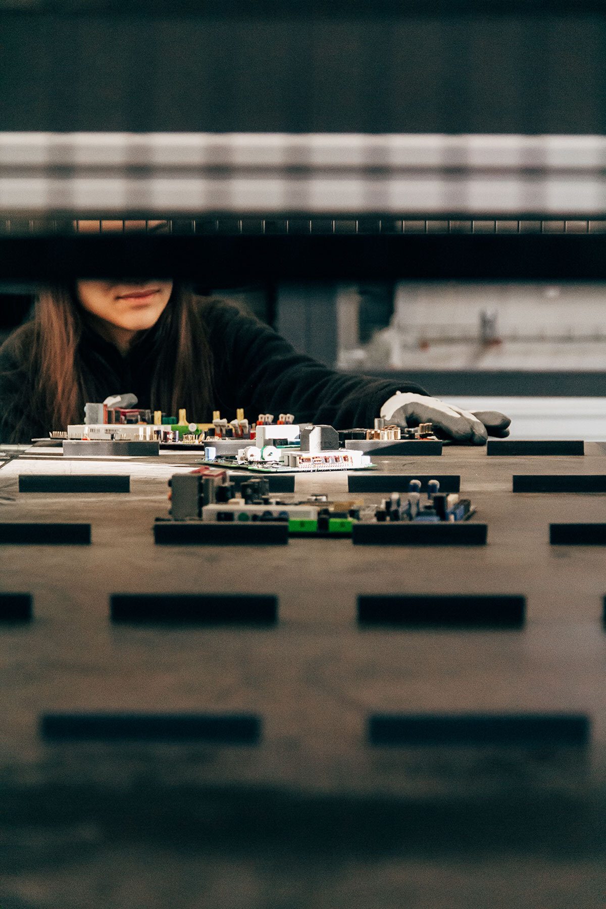 Person in gloves assembling circuit boards, partially obscured by machinery.