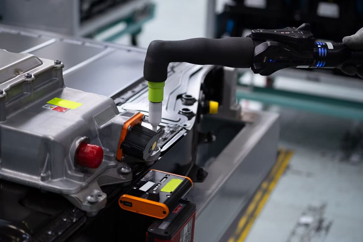Gloved hand uses precision tool to assemble a metallic battery module.