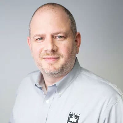 Professional headshot of a bald, bearded man in a gray shirt, smiling.