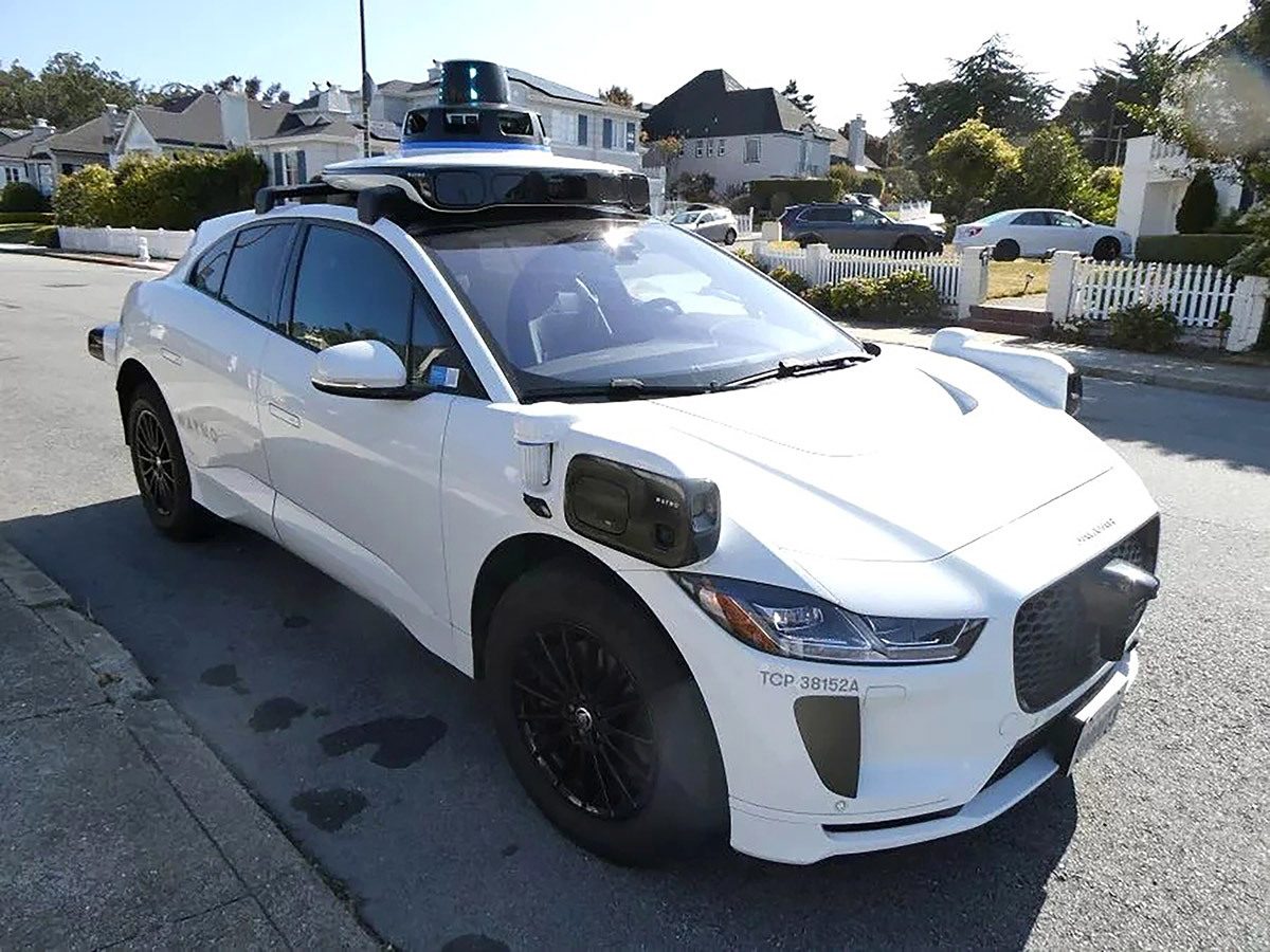 White Waymo self-driving Jaguar I-Pace with roof sensors, parked on a street.