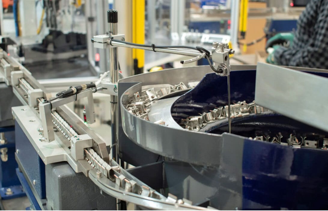 Vibratory bowl feeder sorts metal parts onto a conveyor line.