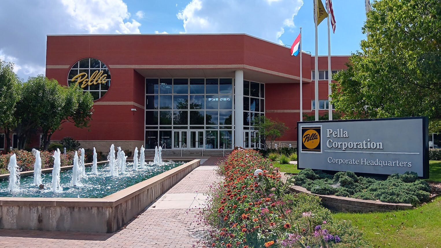 Pella Corporation Headquarters: red brick building, glass, fountain, flags, and company sign.