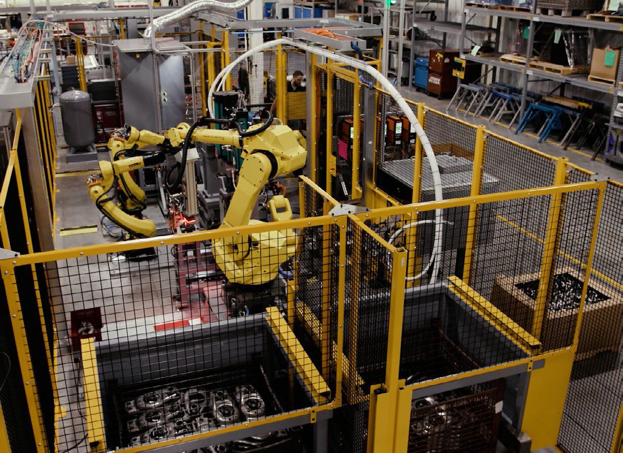 A factory floor with yellow industrial robots processing parts within a safety enclosure.