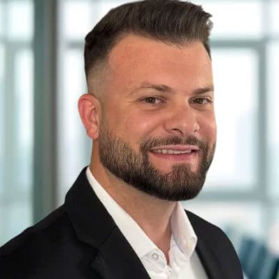 Smiling man with a beard, short hair, and suit jacket.