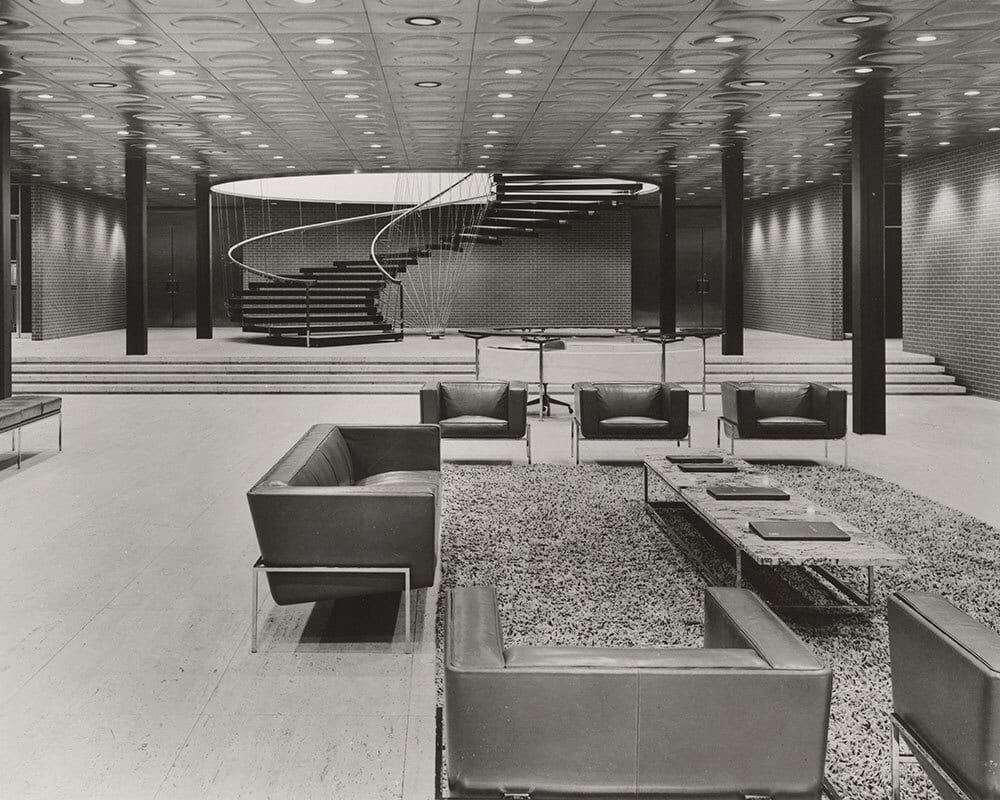 BW photo of a modern lobby featuring a large spiral staircase and multiple seating areas.