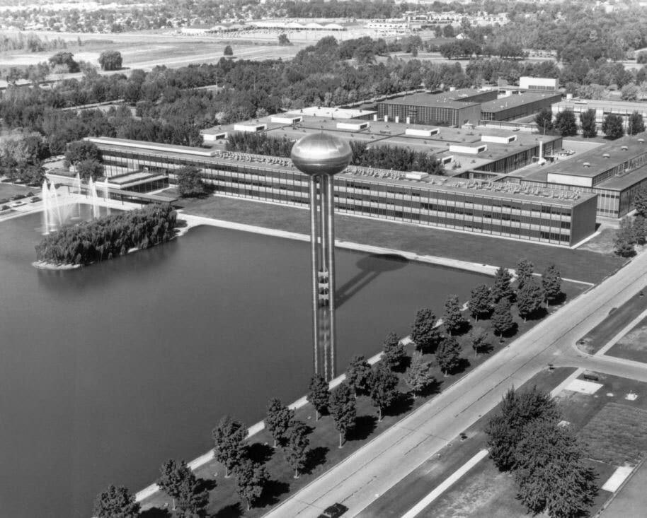 Aerial view of a sprawling corporate campus with a large building, pond, fountains, and a prominent water tower.