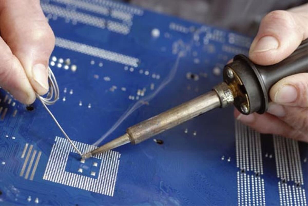 Hands soldering a blue circuit board with a soldering iron and wire.