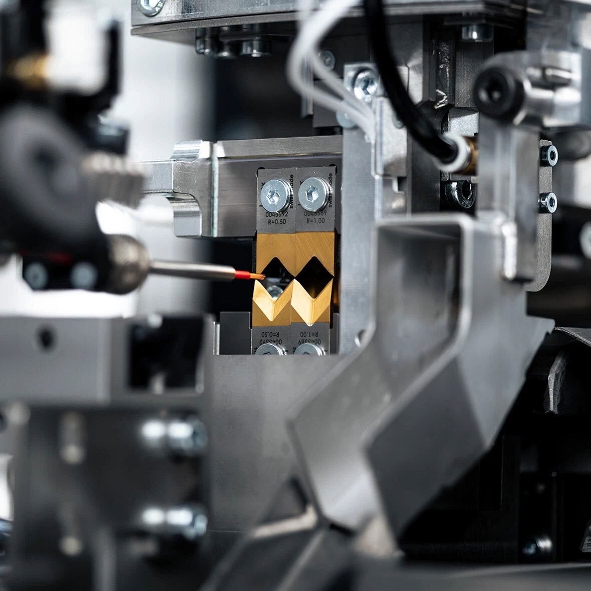 Precision machine inspecting golden V-shaped tools with a red-tipped probe.