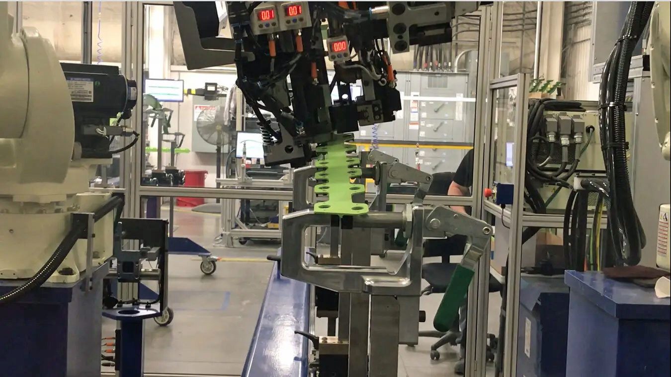 Robot working on a green part held by a metal fixture in a factory.