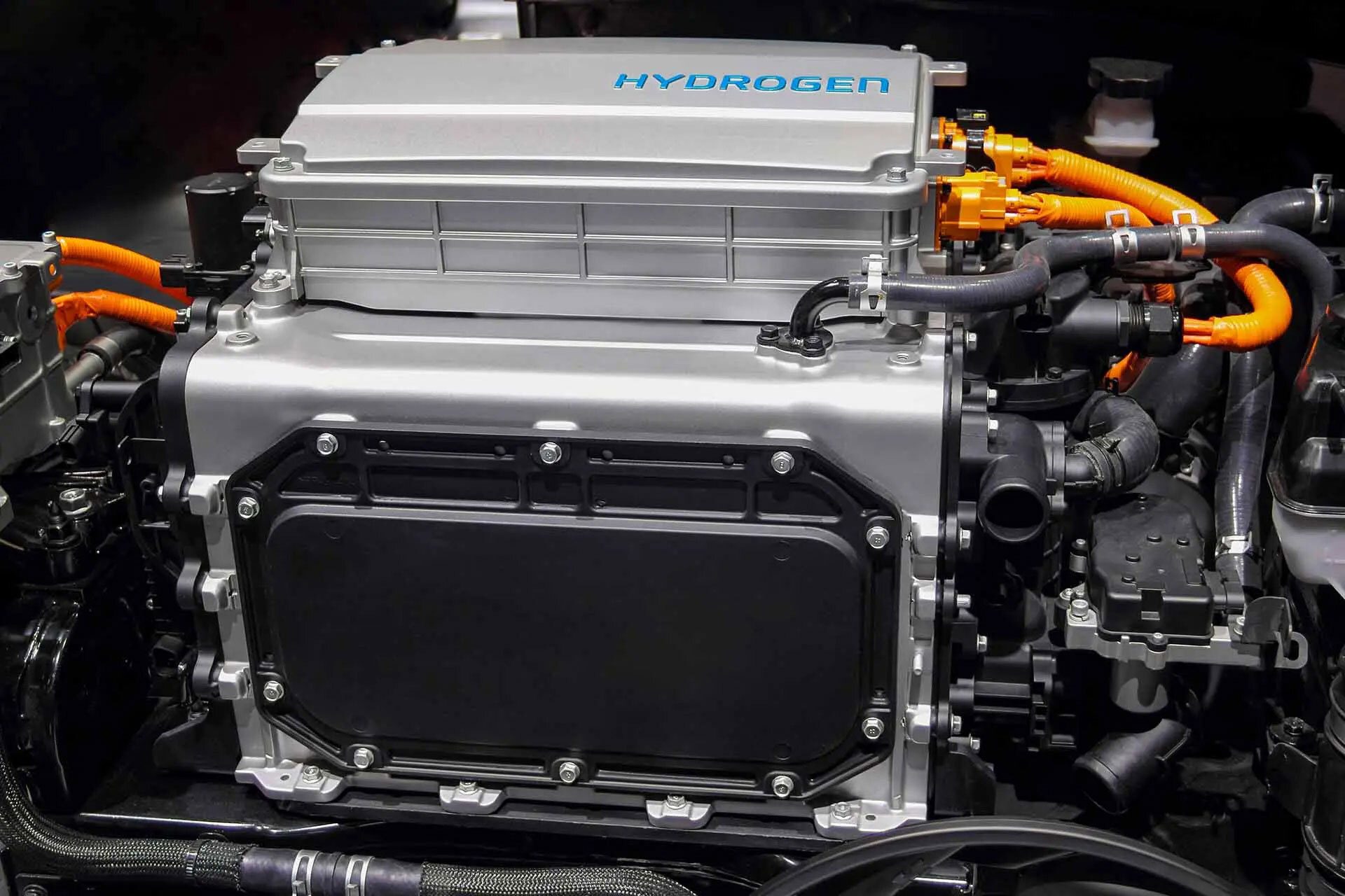 Close-up of a hydrogen fuel cell engine, with "HYDROGEN" text on a silver component and orange cables.