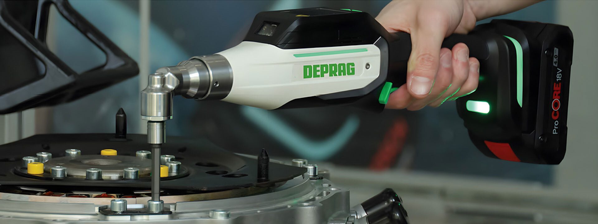 Hand holding a DEPRAG cordless screwdriver, tightening a fastener on an industrial assembly.